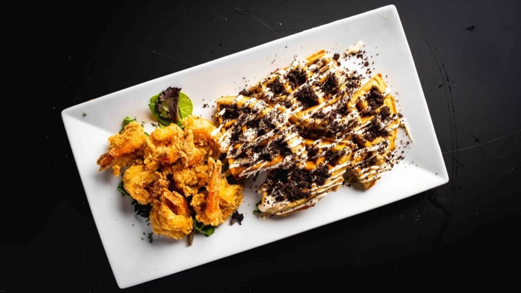 Fried shrimp beside a waffle topped with Oreo crumbs and cream drizzle
